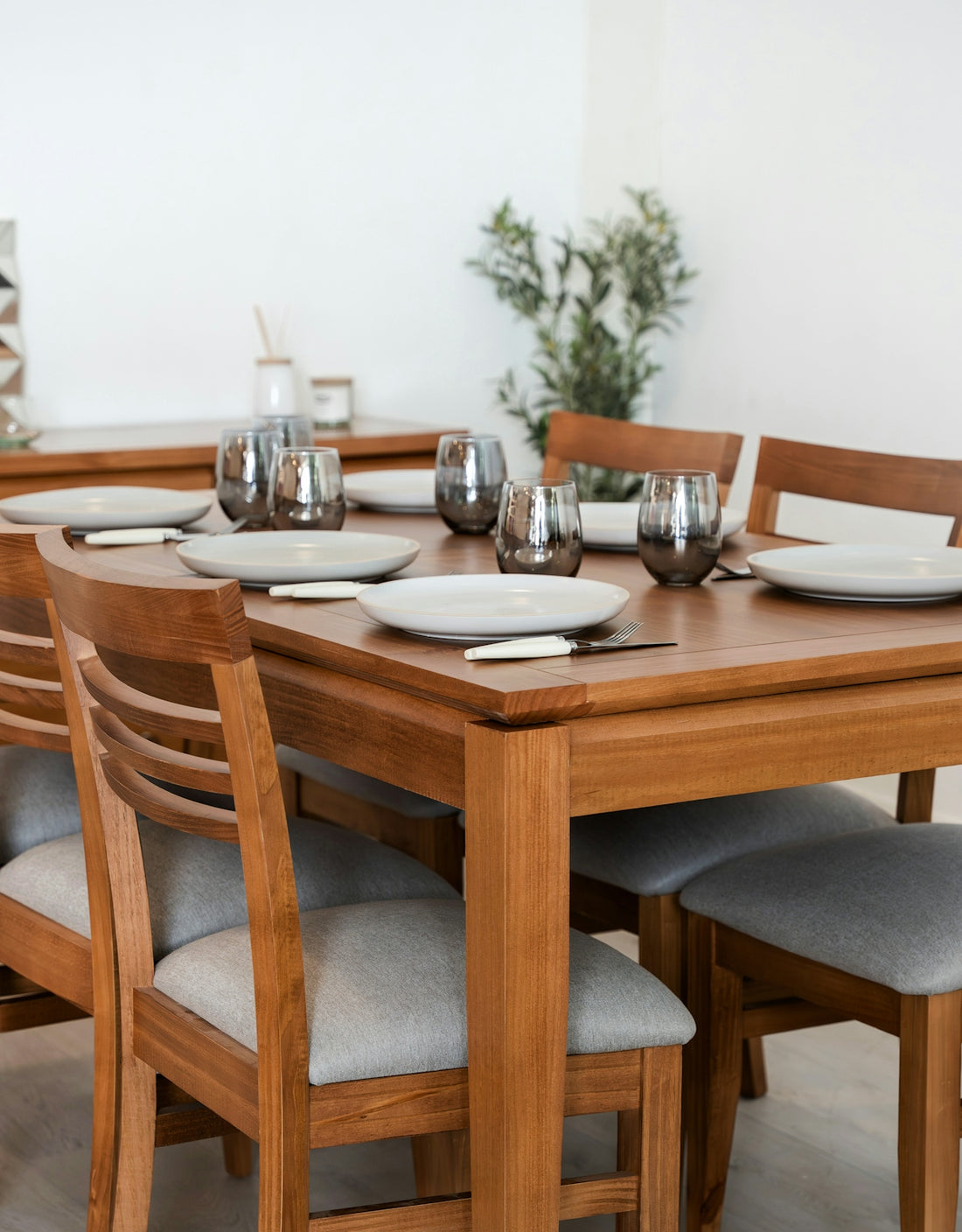 Wooden dining table set with grey chairs and place settings.