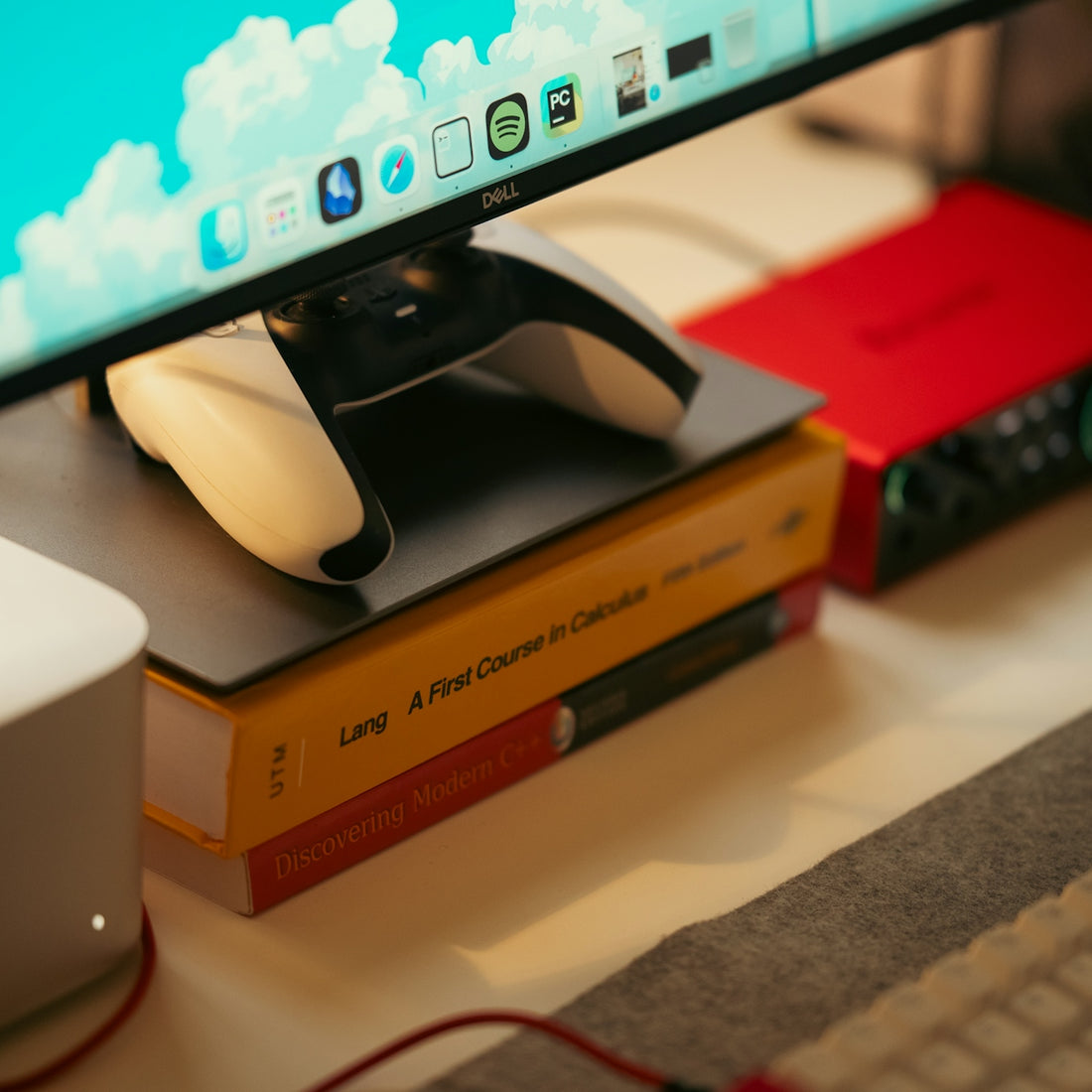 Gaming controller resting on books near computer monitor.