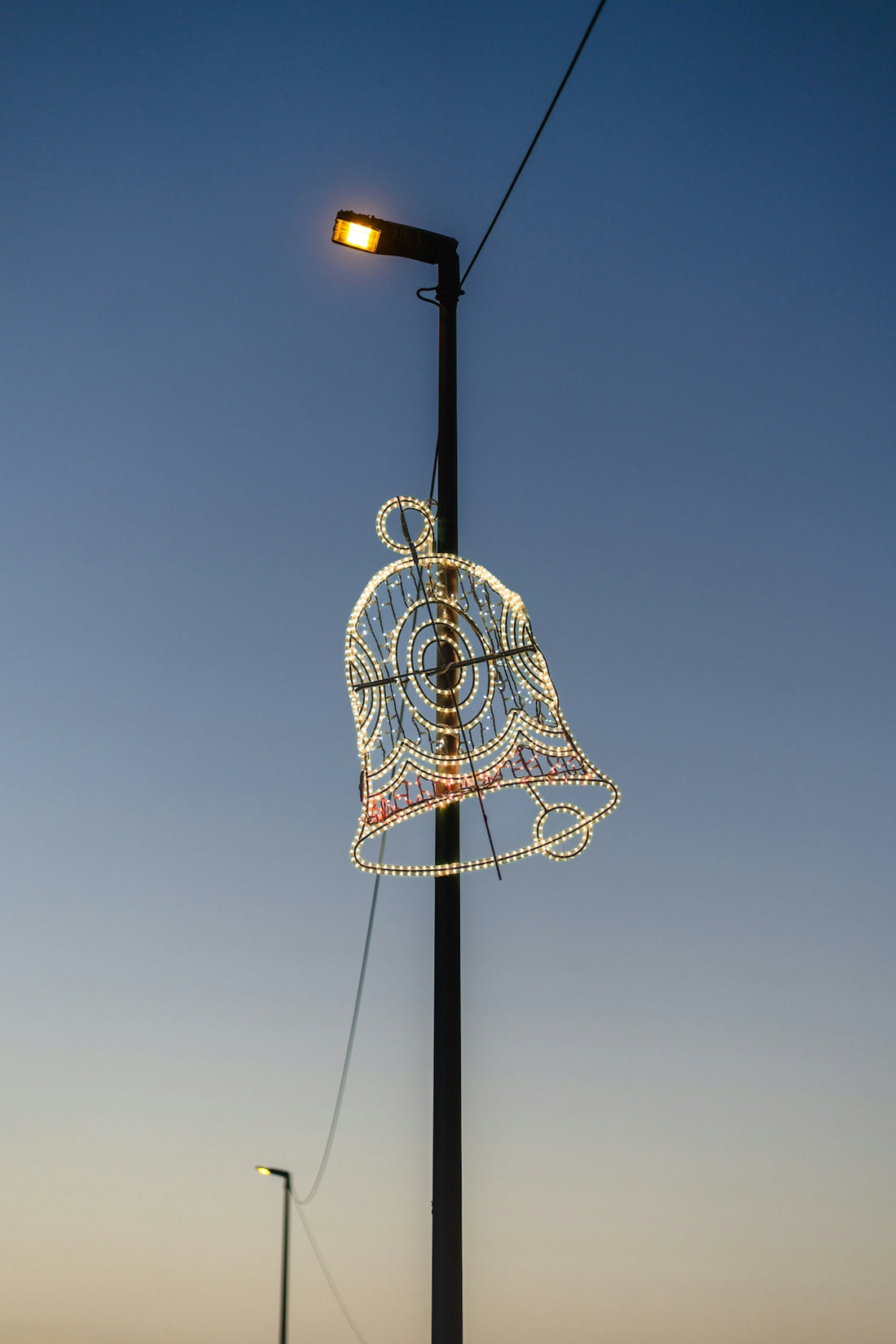 A decorative bell light hangs from a lamppost at dusk.