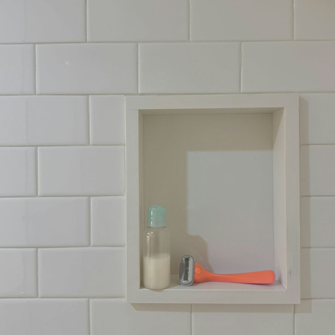 Bathroom niche with a small bottle and orange razor.