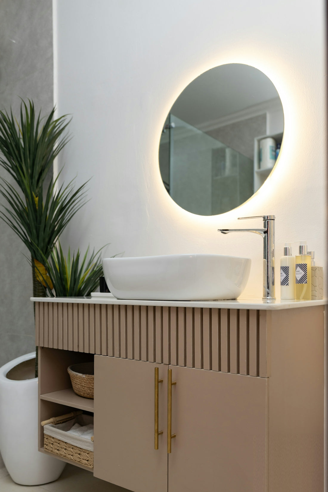 Modern bathroom vanity with round illuminated mirror and vessel sink.